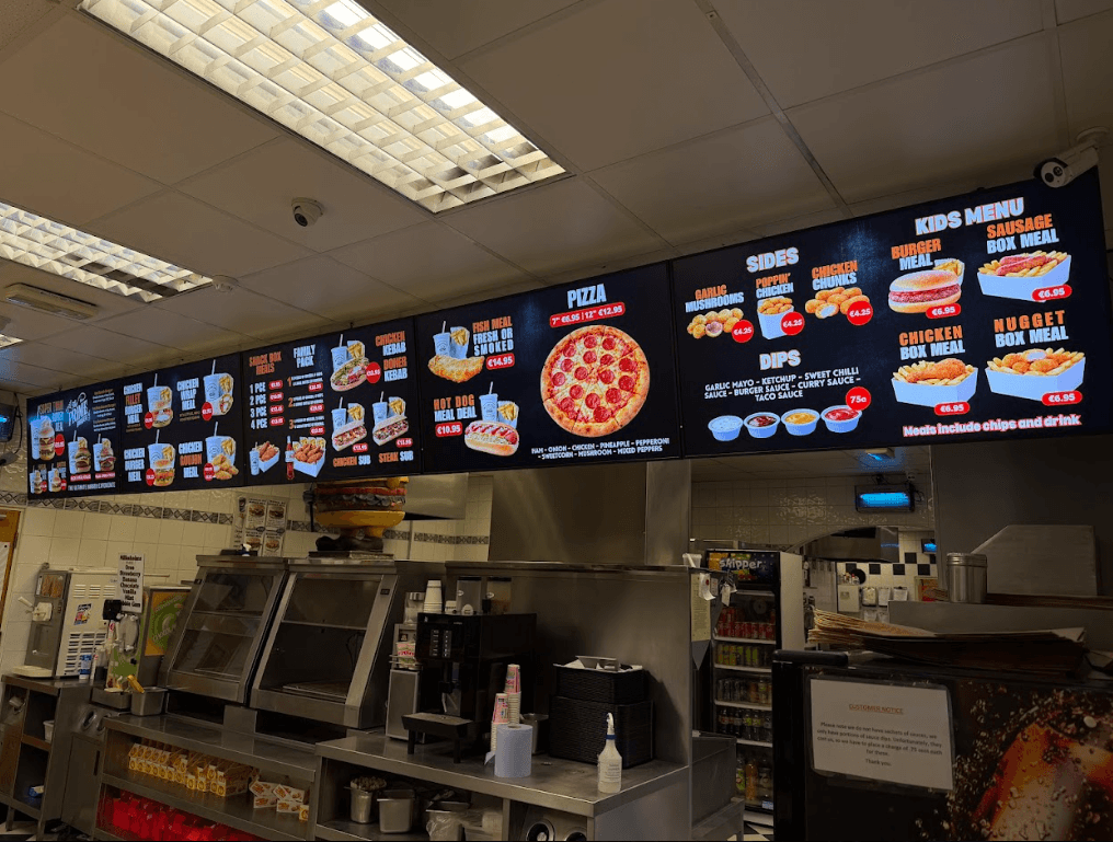 Digital menu boards installed above the counter of a takeaway, running a full food menu